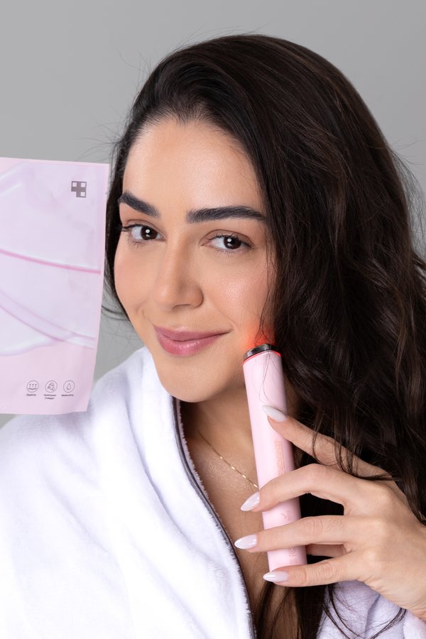 Mulher segurando um aparelho de luz vermelha junto ao rosto durante a rotina de skincare