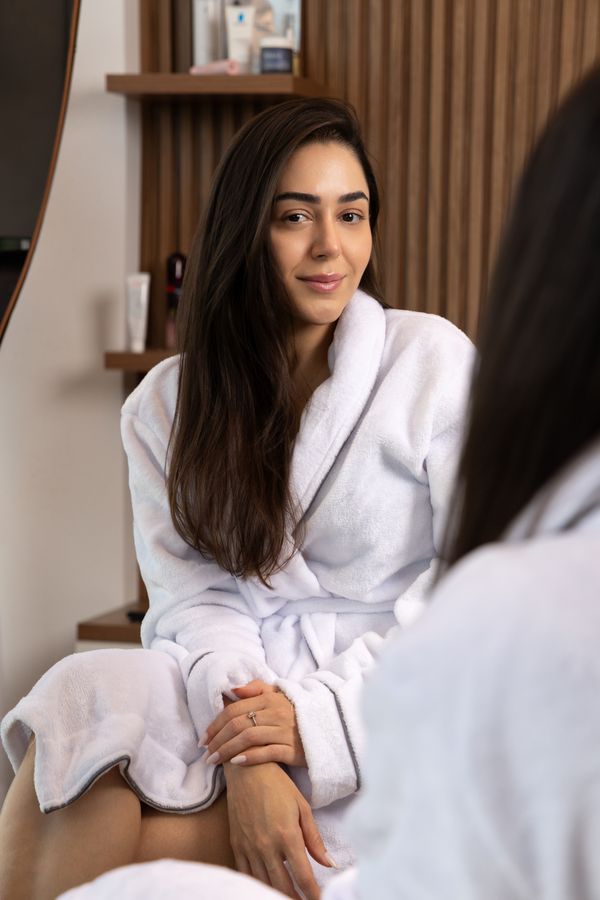 Mulher de roupão sorrindo, relaxada durante sua rotina de cuidados